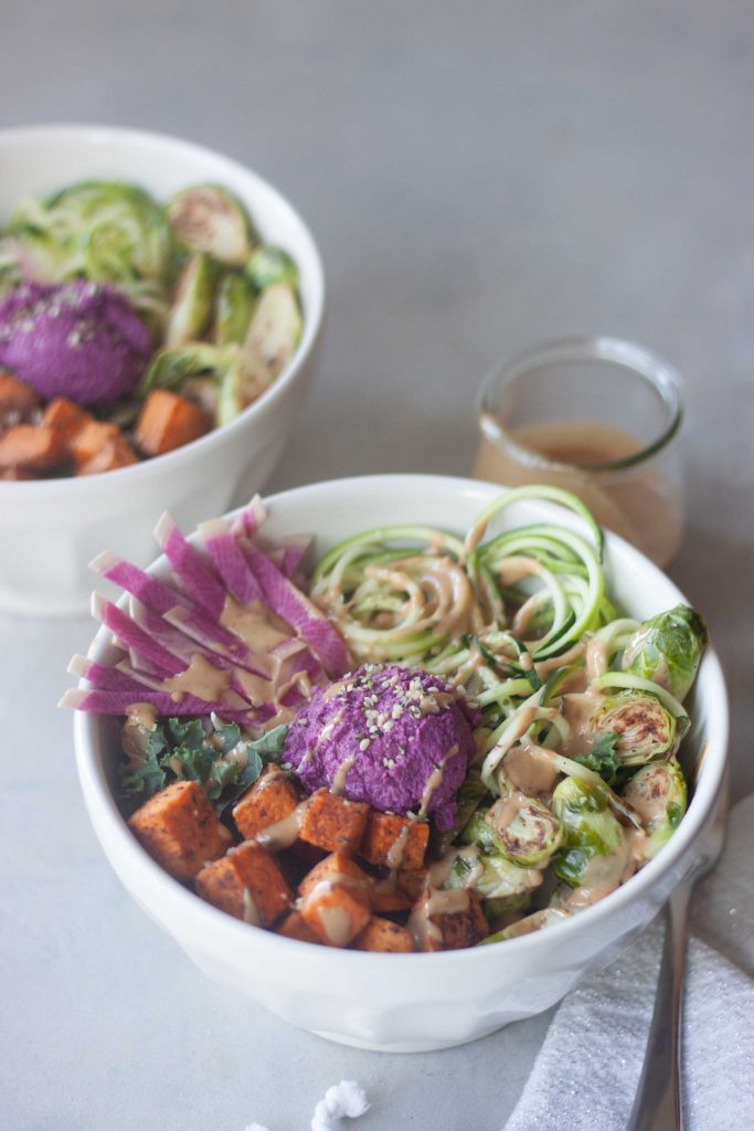 zoodle, purple beet hummus, sweet potato, kale, edamame, brussels, ginger peanut sauce in a bowl