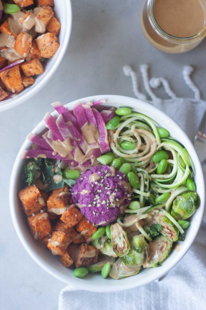 zoodle, purple beet hummus, sweet potato, kale, edamame, brussels, ginger peanut sauce in a bowl