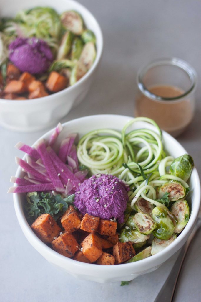 zoodle, purple beet hummus, sweet potato, kale, edamame, brussels, ginger peanut sauce in a bowl