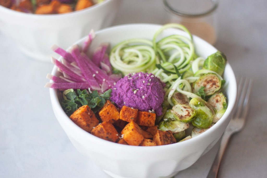 zoodle, purple beet hummus, sweet potato, kale, edamame, brussels, ginger peanut sauce in a bowl