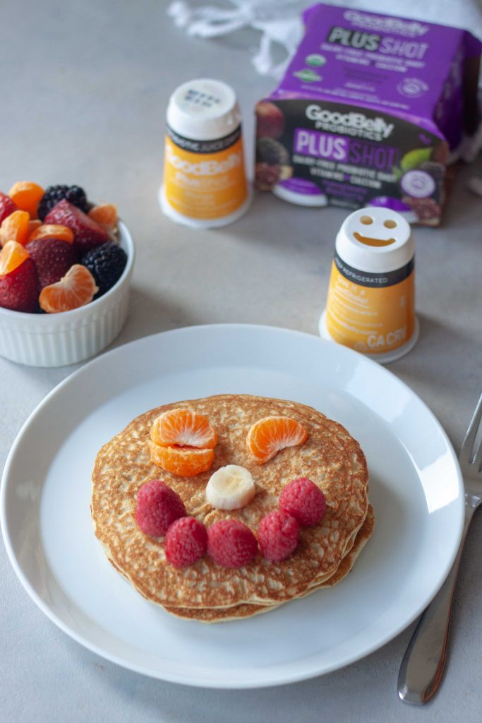 Oatmeal Pancakes topped with a smiley face made of fruit, served with GoodBelly Probiotics.