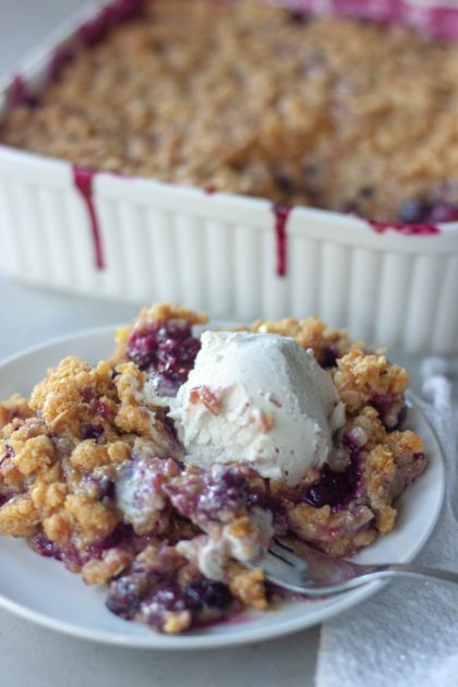 Piece of Sweet Corn Blueberry Crisp topped with ice cream, fork with bite, and pan behind