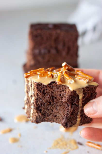 Hand holding Bronana (Brownie Banana) Bread topped with peanut butter and pretzels and bite missing.