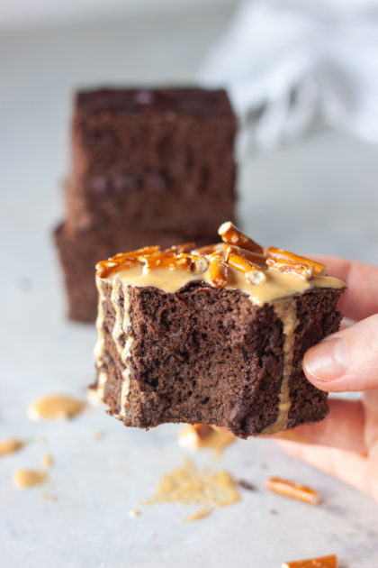 Hand holding Bronana (Brownie Banana) Bread topped with peanut butter and pretzels and bite missing.