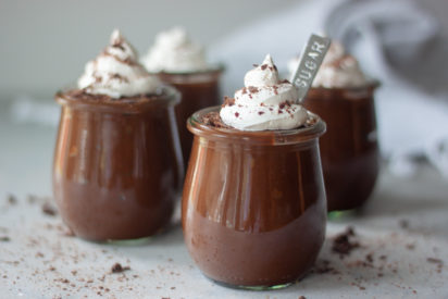 Glass jars with chocolate avocado pudding, whip cream, chocolate, and spoon